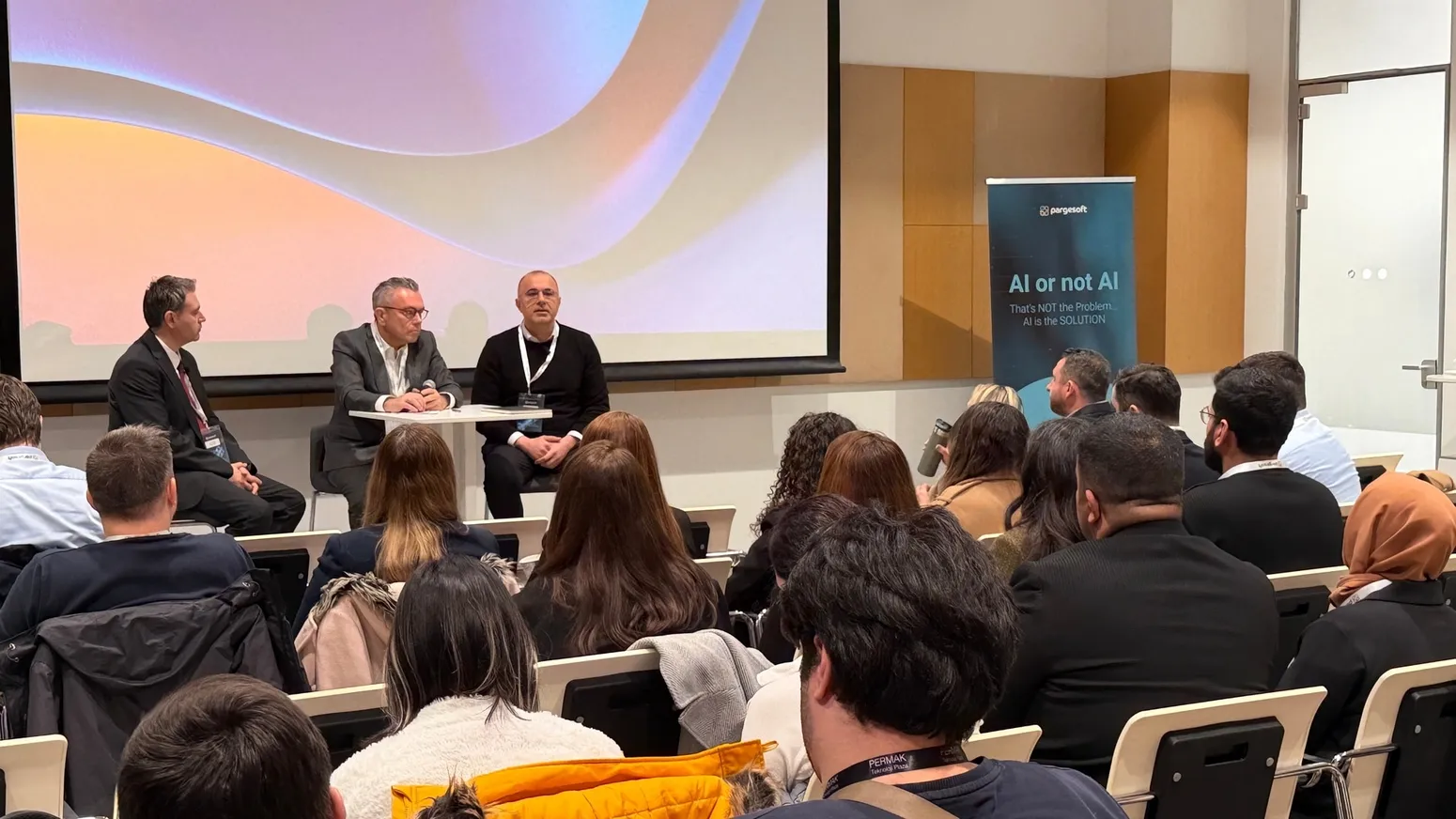 Sahnede üç kişilik panel konuşması yapılırken izleyicilerin arkadan görünümü