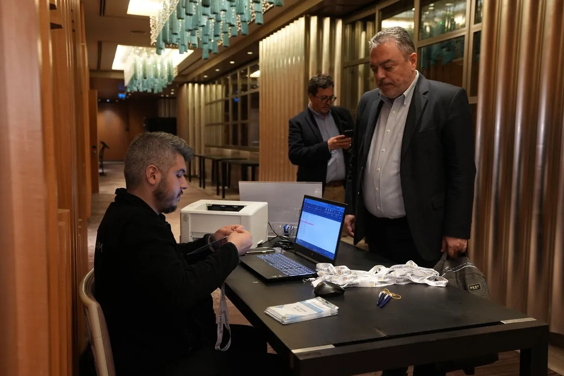 Etkinlik kayıt masasında dizüstü bilgisayar başında oturan görevli, masada Pargesoft yaka kartları