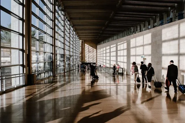 Güneş ışığı alan cam cepheli terminal koridorunda valizleriyle yürüyen iş insanları