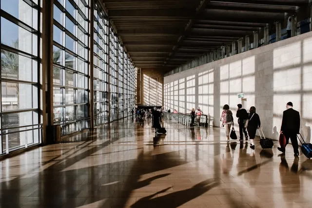 Güneş ışığı alan cam cepheli terminal koridorunda valizleriyle yürüyen iş insanları