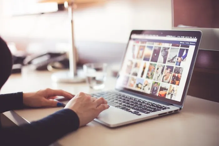 Laptop ekranında fotoğraf galerisi görünürken klavyede yazan bir çift el.