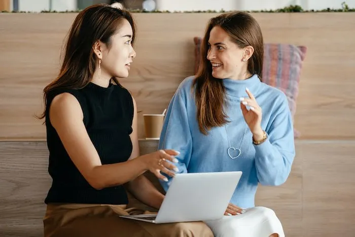Ahşap kaplamalı bir ortamda laptopla oturan iki kadının sohbet etmesi.