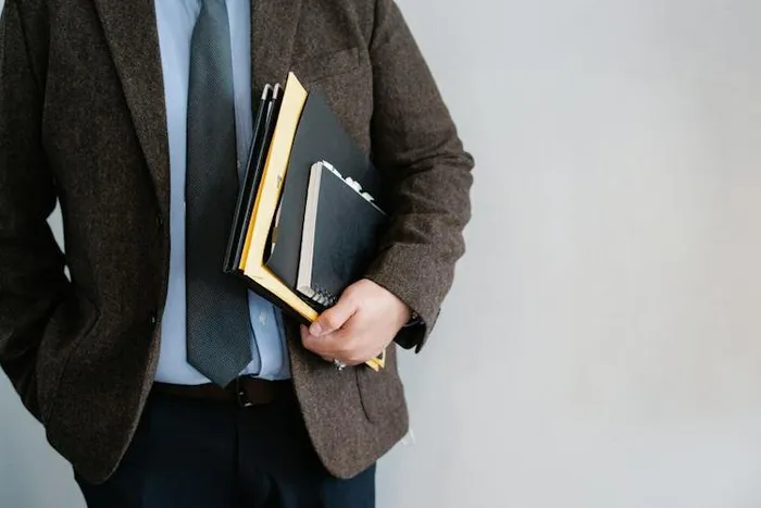 Takım elbiseli bir kişinin kolunun altında birkaç defter ve dosya taşıması.