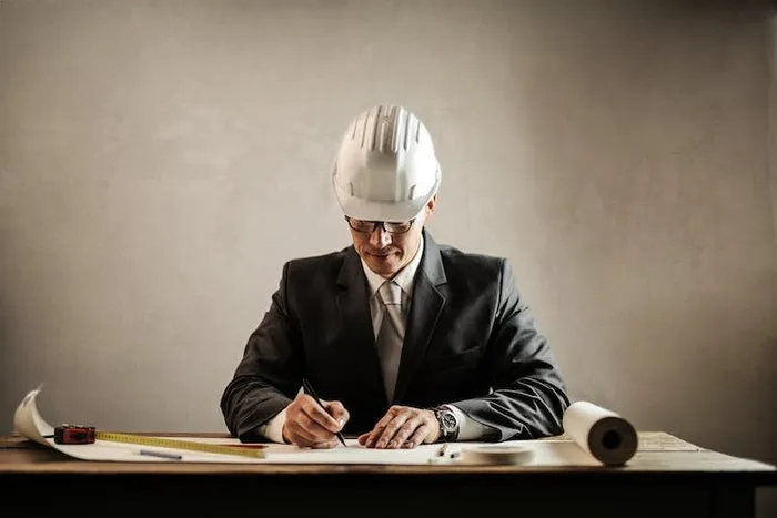 Baret takan bir mühendis, masasındaki mimari plan üzerinde kalemle işaretleme yapıyor.