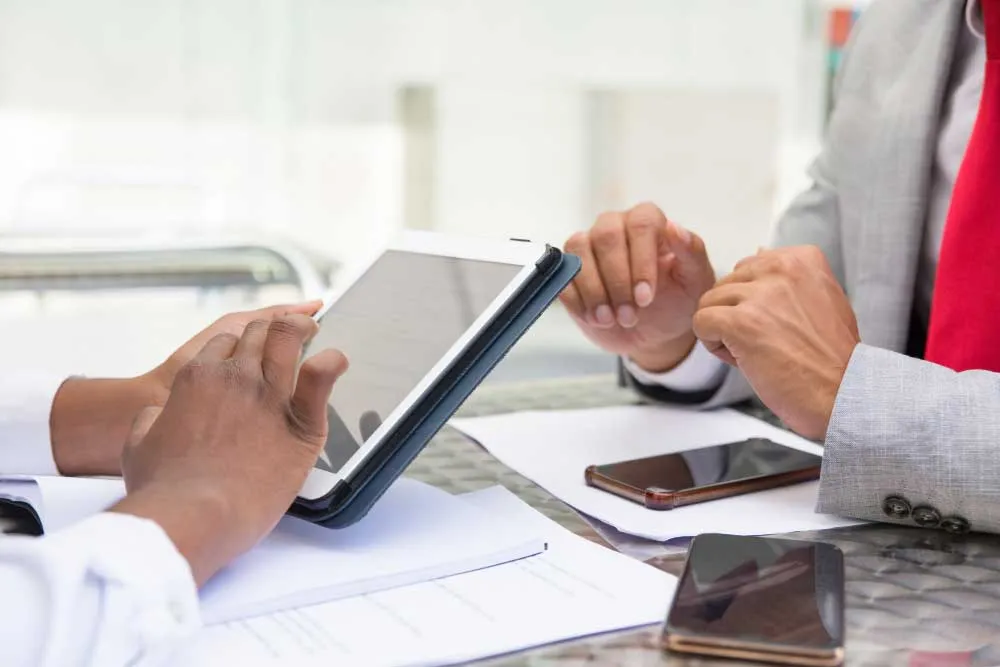 Toplantı masasında tablet üzerinde birlikte çalışan iki iş insanının elleri