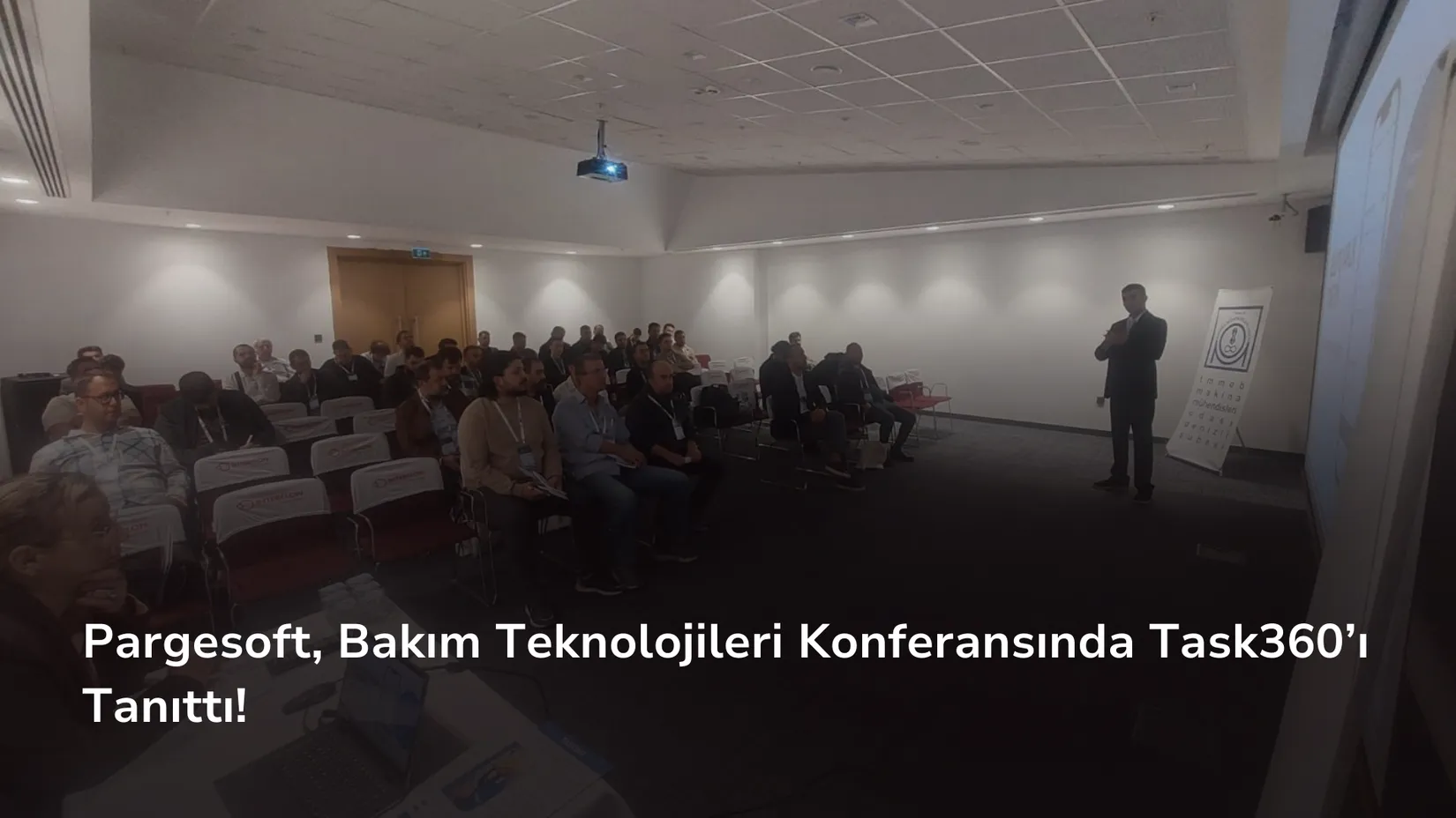Konferans salonunda oturan katılımcılar ve önde ayakta sunum yapan bir konuşmacı