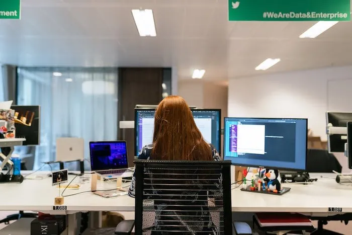 Bir kadın arkadan görünüyor; iki ekranından birinde kod editörü açık, üstte '#WeAreData&Enterprise' pankartı var.