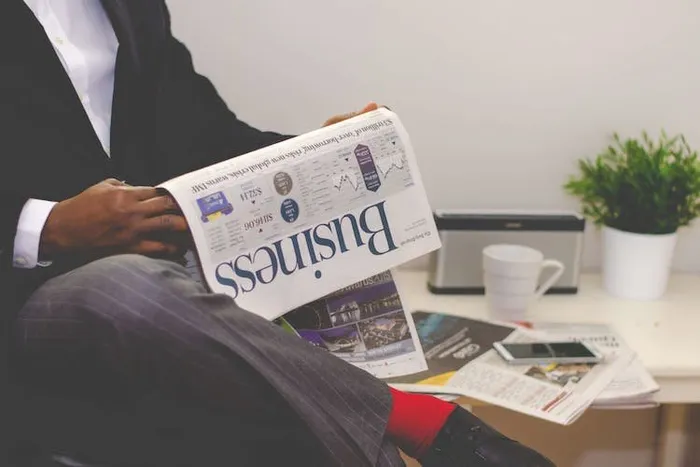Takım elbiseli bir kişinin 'Business' yazılı bir gazete okuduğu masa başı çekim