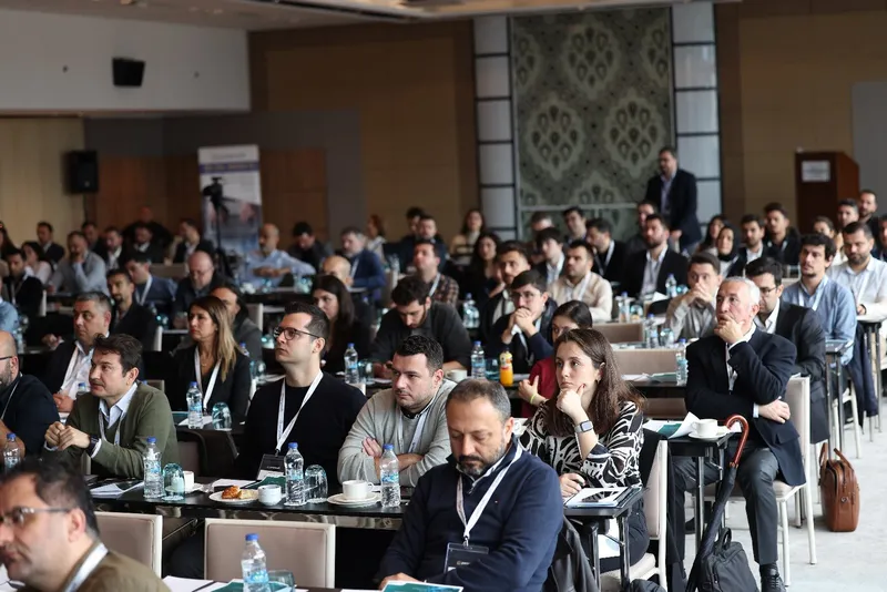 Konferans salonunda masalarda oturan kalabalık bir dinleyici grubu