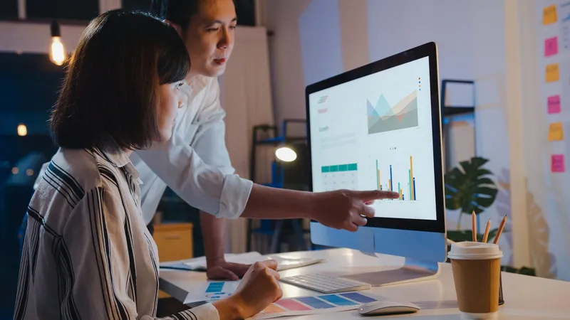 Ofiste iki kişi, masaüstü ekranındaki çizgi ve sütun grafikleri içeren paneli inceliyor