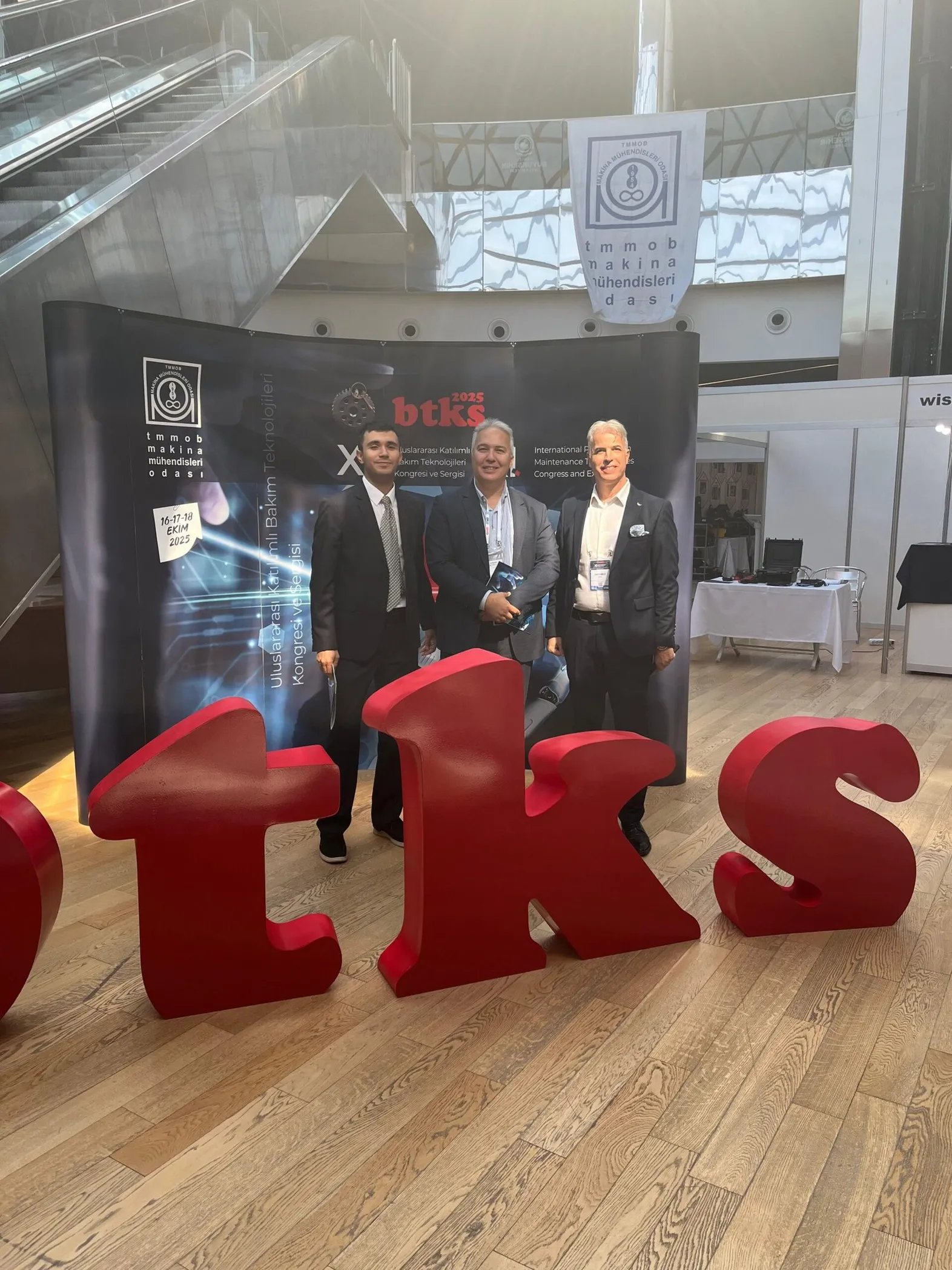BTKS 2025 standı önünde üç kişinin, kırmızı büyük 'TKS' harfleri arka planında çektirdiği fotoğraf