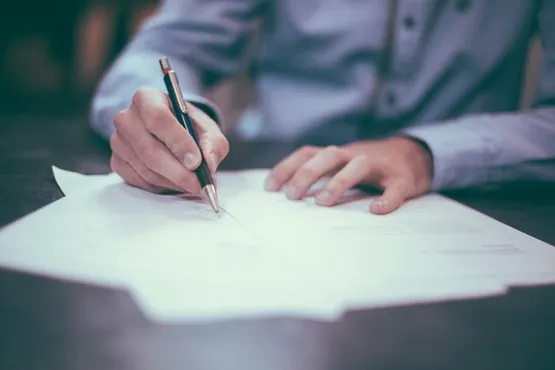 Close-up of a person writing on paper with a pen at a desk