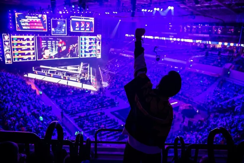 Dev ekranlı büyük bir arenada kalabalığın önünde kolunu havaya kaldırmış bir kişinin silüeti